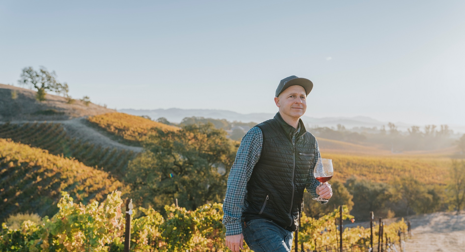 Copain Winemaker, Ryan Zepaltas, walking in the Vineyard holding a glass of Copain red wine.